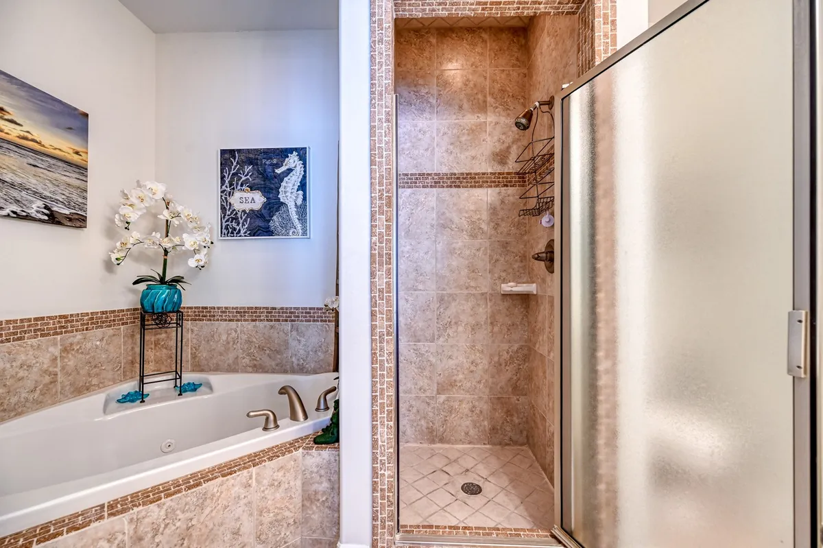 A serene bathroom featuring a luxurious jacuzzi tub, a spacious shower area, elegant framed artwork, and an orchid plant. The space exudes a spa-like ambiance perfect for unwinding and self-care routines.