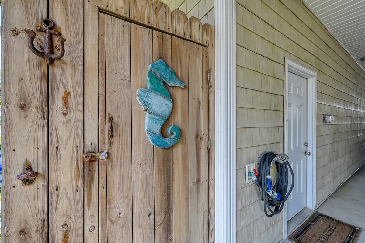 The entryway displays playful coastal decor, including a seahorse ornament and anchor details, suggesting a friendly, welcoming first impression. The wooden gate and visible door handle evoke the excitement of arriving at a beach house ready for group adventures.