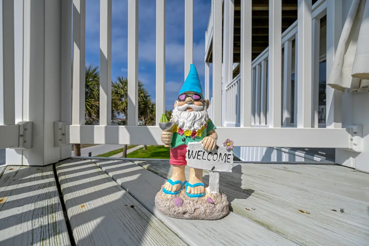 A welcoming exterior entryway with a garden gnome, a prominent 'Welcome' sign, wooden decking, and lush palm trees. The space feels friendly and inviting, setting the tone for arrival.