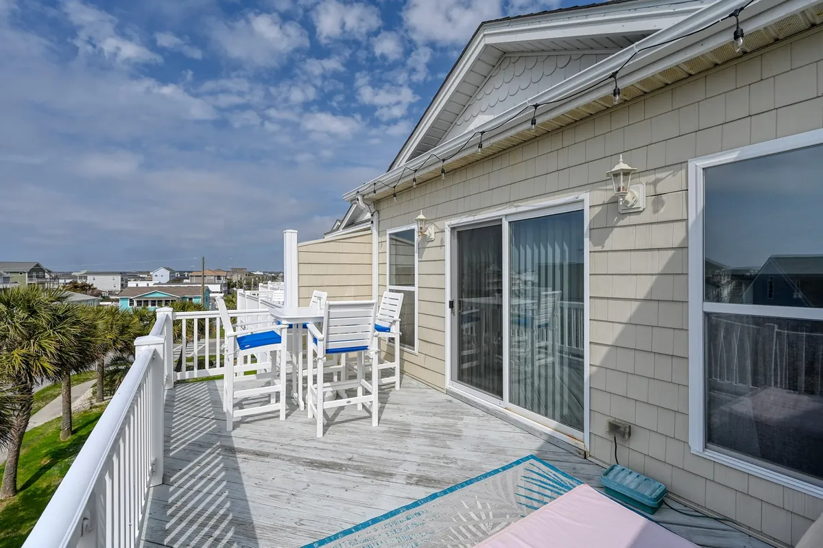 This exterior shot shows a tranquil deck with comfortable seating, surrounded by palm trees and neighboring coastal homes. The setting evokes the laid-back atmosphere of a beach community and suggests both privacy and the opportunity to socialize, with views that invite guests to enjoy the coastal breeze and evening sunsets.