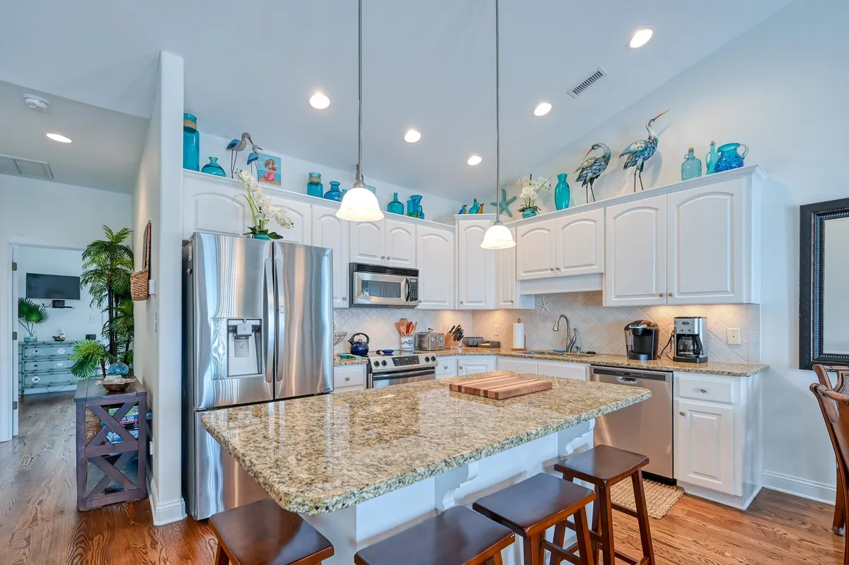 A warm, contemporary kitchen centered around a granite island, with sleek stainless steel appliances, decorative teal accents, and stylish pendant lighting. The space is designed for gathering, with ample countertop space for meal prep and conversation.