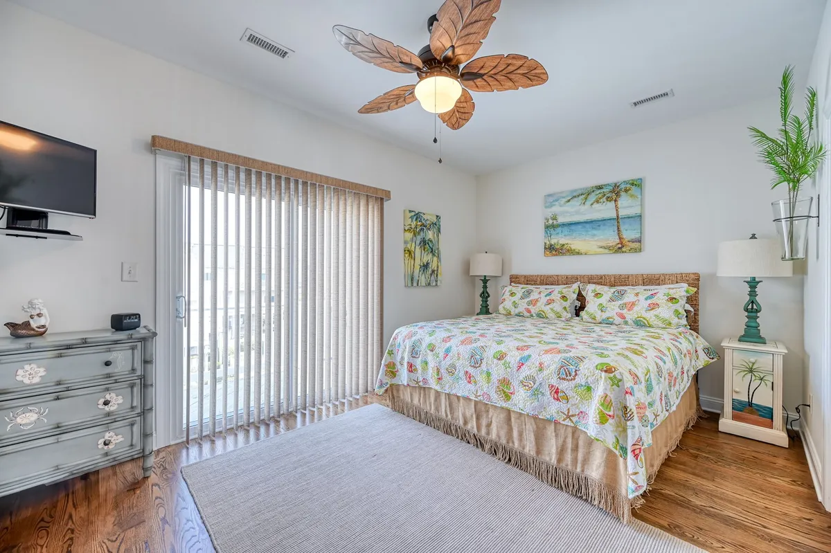 A cheerful, inviting bedroom featuring a bed with colorful bedding, a ceiling fan with a leaf design, decorative wall art, and a charming dressing table. Soft natural light streams in, creating a comfortable and relaxing atmosphere ideal for restful nights.