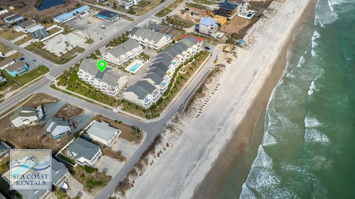 A sweeping exterior view featuring beachfront properties, a shimmering swimming pool, and the ocean's waves rolling onto the sandy shore. The scene exudes laid-back coastal energy, highlighting both active and relaxing outdoor spaces.