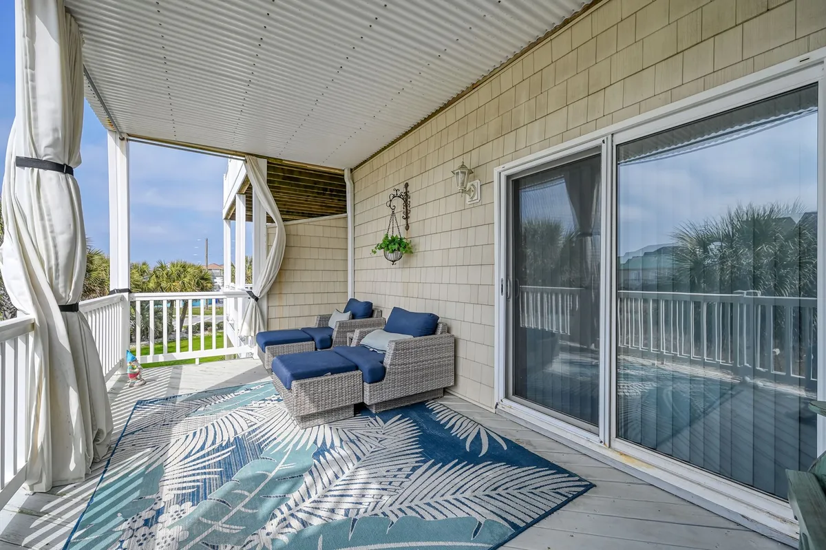 This image features a welcoming outdoor seating area complete with comfortable chairs, a decorative rug, and a planter with greenery. The arrangement suggests a space ideal for relaxing with morning coffee, sharing stories with friends in the evening, or simply taking in the fresh air close to the beach.