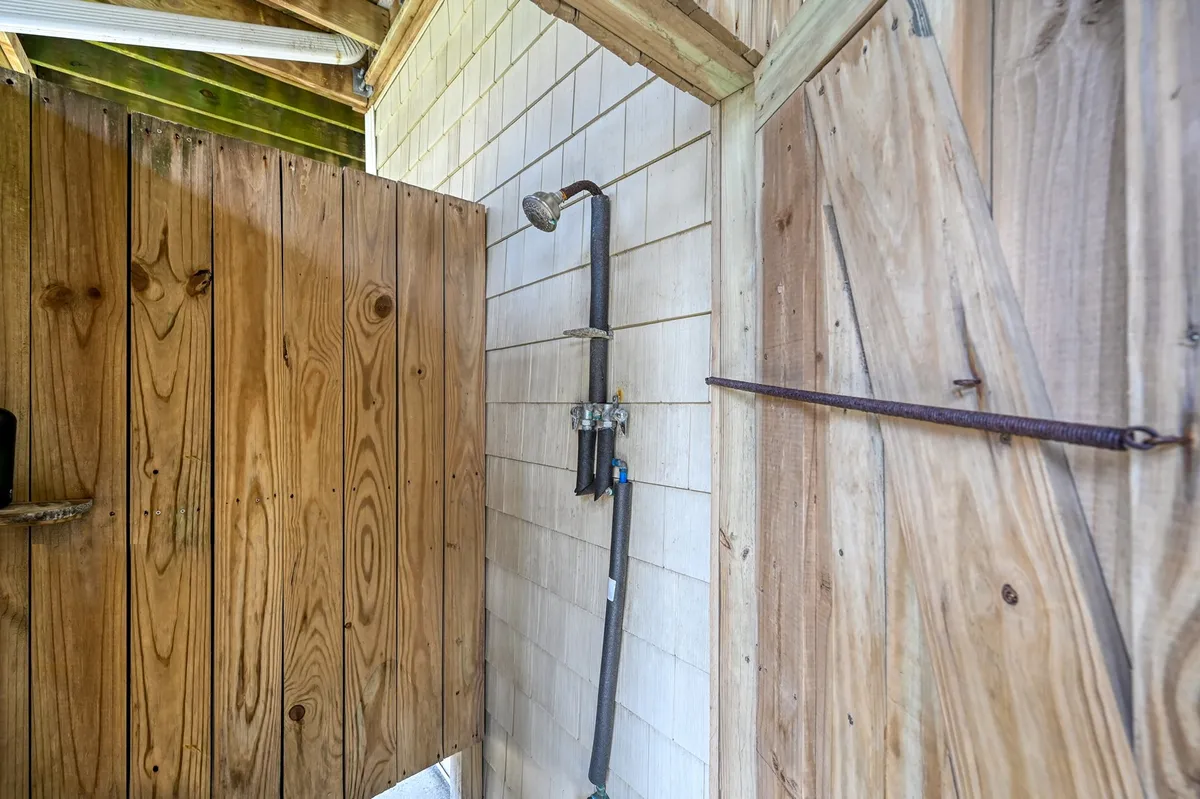An inviting outdoor shower with rustic wooden walls and a simple fixture. The design is open and practical, evoking a sense of cleansing and relaxation after a day at the beach.