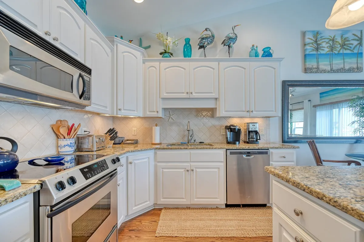 A bright, friendly kitchen interior with stainless steel appliances, a granite countertop, decorative bird figurines, and bright blue accents. The space is designed for cooking, entertaining, and family gatherings, with a welcoming atmosphere.