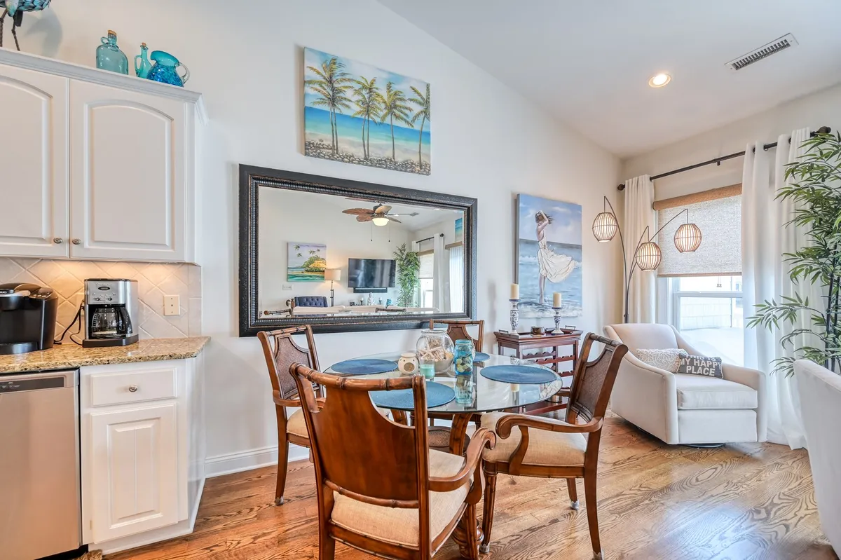 A bright and cheerful dining area with a large table surrounded by comfortable seating, accented by a large mirror and decorative artwork. The setting suggests plenty of space for group meals, socializing, and enjoying the view.
